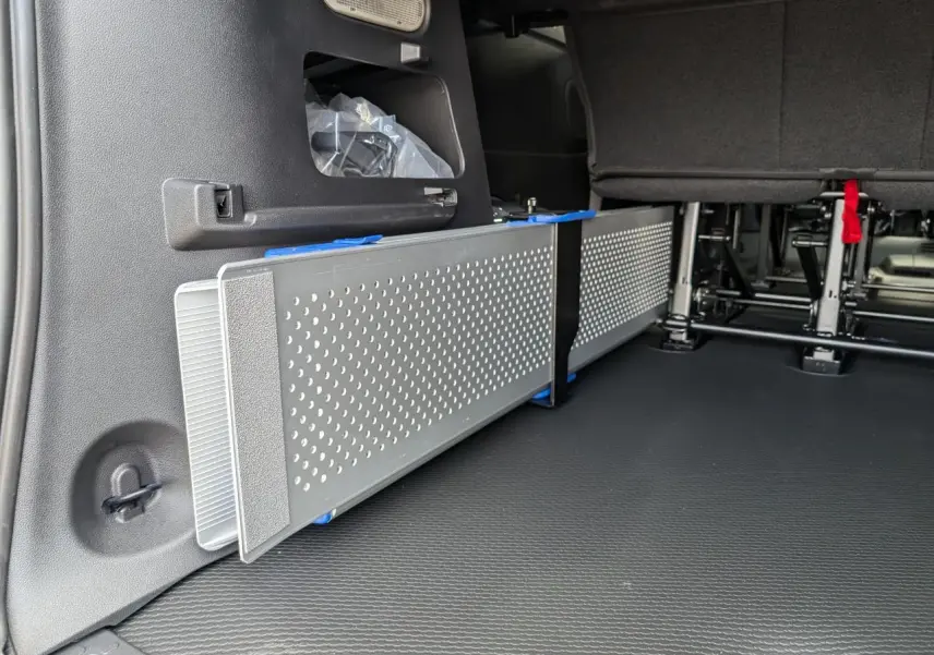 Vue intérieure du coffre arrière du Renault Trafic Fourgon gris, montrant une rampe amovible en aluminium ajouré côté gauche.