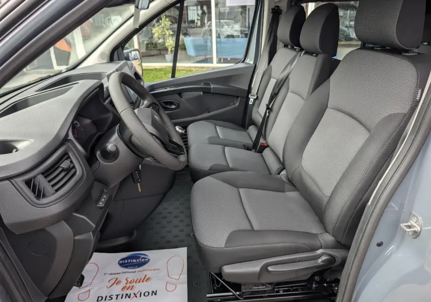 Vue intérieure côté conducteur du Renault Trafic Fourgon 2025, sièges tissu gris Kompo Black et tableau de bord noir.