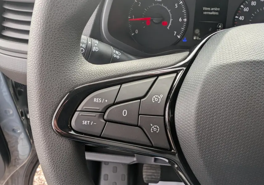 Gros plan sur les commandes au volant à gauche du Renault Trafic Fourgon gris, avec tableau de bord et compte-tours visibles.