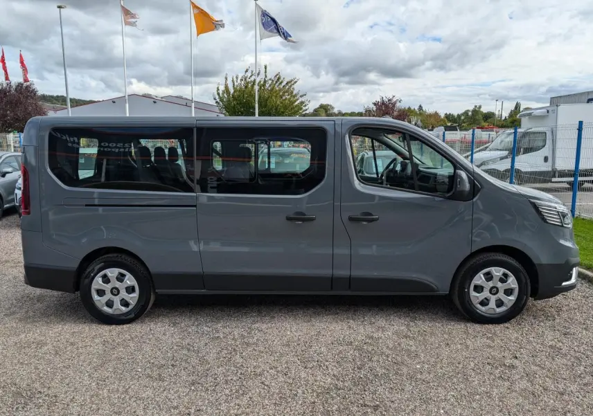 Profil droit d’un Renault Trafic Fourgon L2 gris avec vitres latérales et jantes argentées, stationné en extérieur.