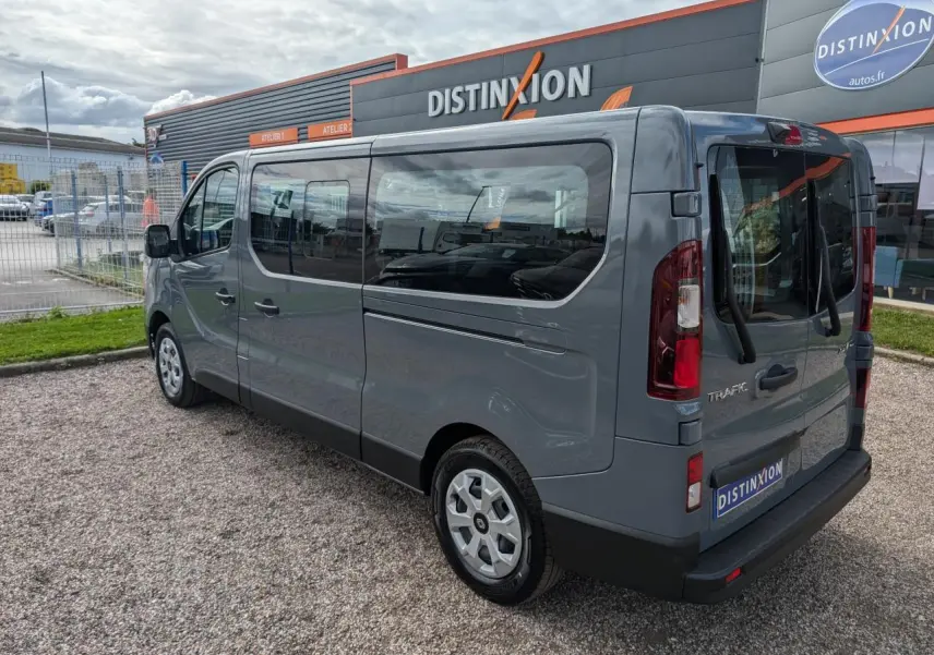 Vue 3/4 arrière droite du Renault Trafic Fourgon gris avec vitres latérales et jantes avec enjoliveurs sur parking.