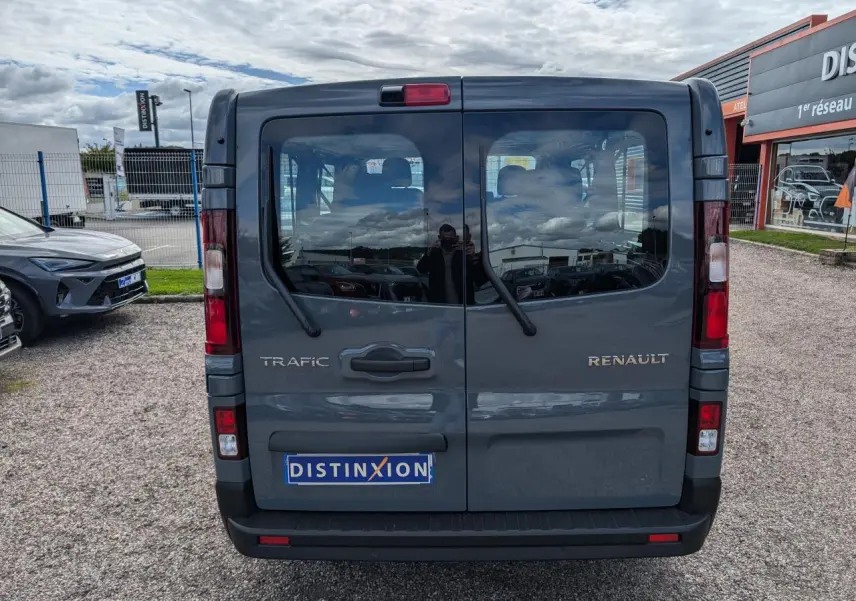 Vue arrière d'un Renault Trafic Fourgon gris avec portes battantes et logo distinctif sur parking.
