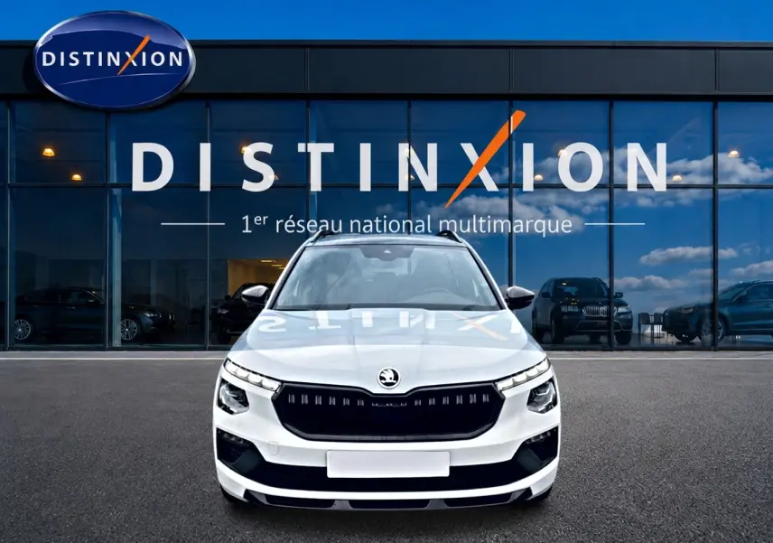 Vue de face d'un Skoda Kamiq blanc nacré avec calandre noire, devant une vitrine Distinxion.
