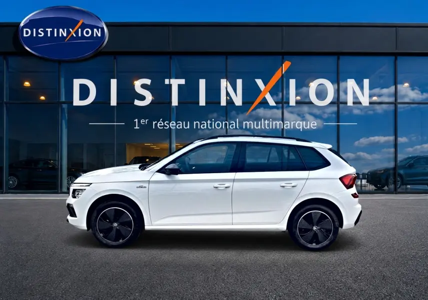 Vue de profil côté gauche d'un Skoda Kamiq blanc nacré avec jantes noires devant une vitrine Distinxion.