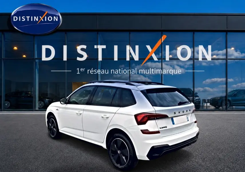 Vue 3/4 arrière droite du Skoda Kamiq blanc nacré avec jantes noires et toit panoramique, devant une vitrine Distinxion.