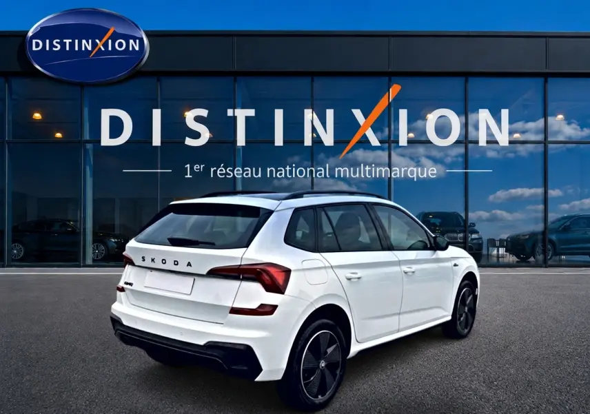 Vue 3/4 arrière droite d'un Skoda Kamiq blanc nacré avec jantes noires, devant une vitrine Distinxion.