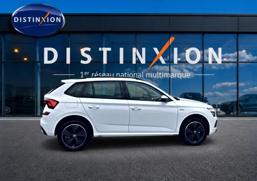 Vue latérale droite d'un Skoda Kamiq blanc nacré avec jantes noires devant une vitrine Distinxion.