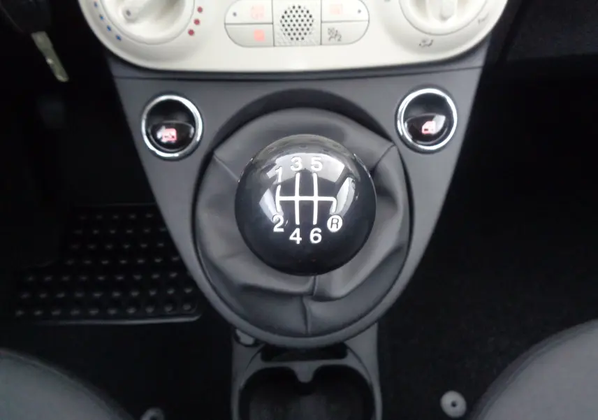 Gros plan sur le levier de vitesses manuel noir de la Fiat 500 blanche, entouré de commandes centrales et console noire.