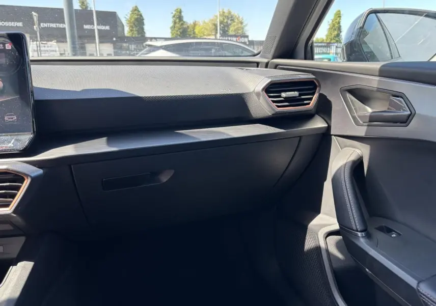 Vue intérieure côté passager du tableau de bord et de la portière d'une CUPRA Leon Sportstourer 2024 avec finitions noires et inserts cuivrés.