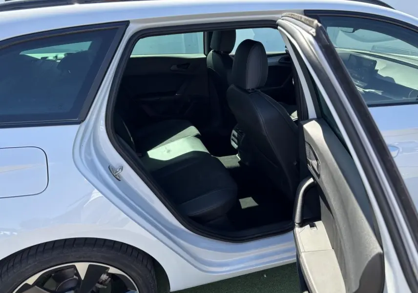 Vue côté gauche arrière d'une CUPRA Leon Sportstourer blanc Nevada, porte ouverte révélant l'intérieur noir et les jantes alliage 18 pouces.