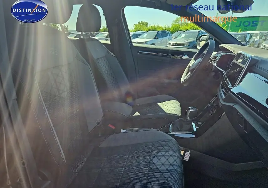 Vue intérieure côté conducteur du Volkswagen T-Roc 2025 avec sièges tissu noir et volant multifonction sport.