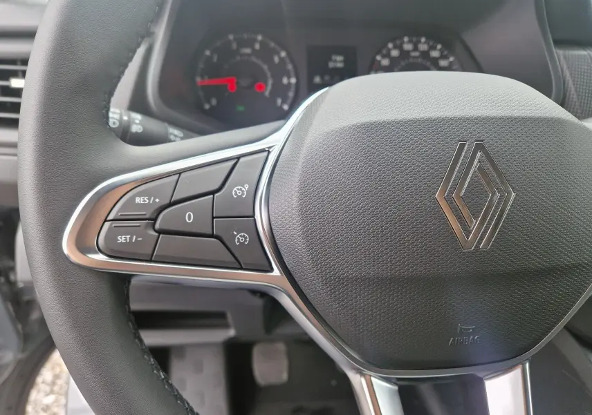 Gros plan sur le volant noir du Renault Trafic Fourgon 2025 avec commandes intégrées et logo Renault central argenté.