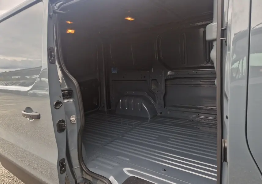 Vue latérale gauche du Renault Trafic Fourgon gris urbain 2025, montrant l’espace de chargement vide avec porte coulissante ouverte.