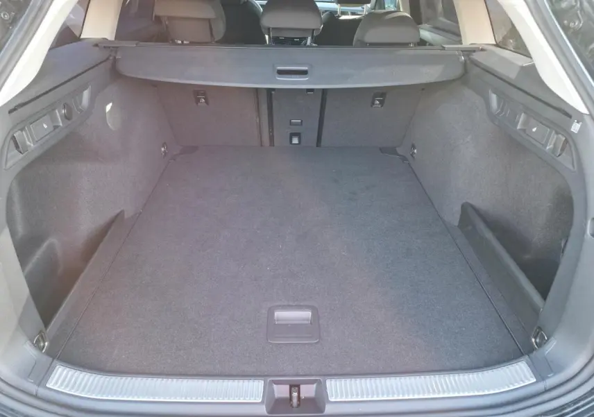 Coffre spacieux ouvert de la Volkswagen Passat SW noire 2024, avec plancher plat et revêtement textile gris.