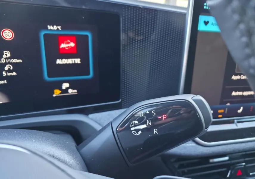 Gros plan sur le levier de vitesses noir brillant de la Volkswagen Passat SW 2024, avec écran tactile en arrière-plan.