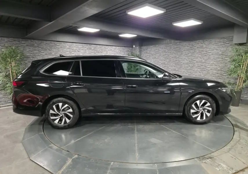 Volkswagen Passat SW noire vue de profil côté gauche, avec jantes alliage et vitres teintées, en intérieur showroom.