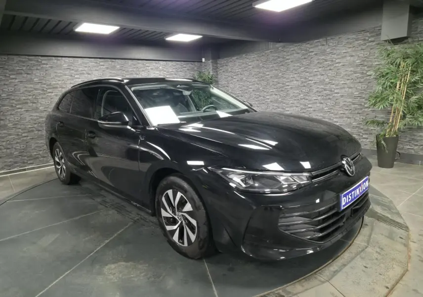 Volkswagen Passat SW noire vue 3/4 avant droit en intérieur avec jantes alliage et phares LED allumés.