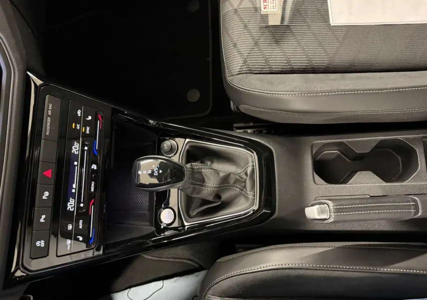 Vue rapprochée de la console centrale du Volkswagen T-Cross 2024, avec levier de vitesse automatique et sièges tissu gris.