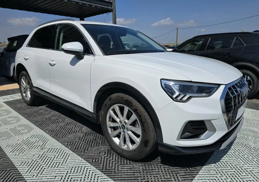 Audi Q3 blanc vue 3/4 avant droit, avec calandre hexagonale et jantes aluminium 5 branches doubles.