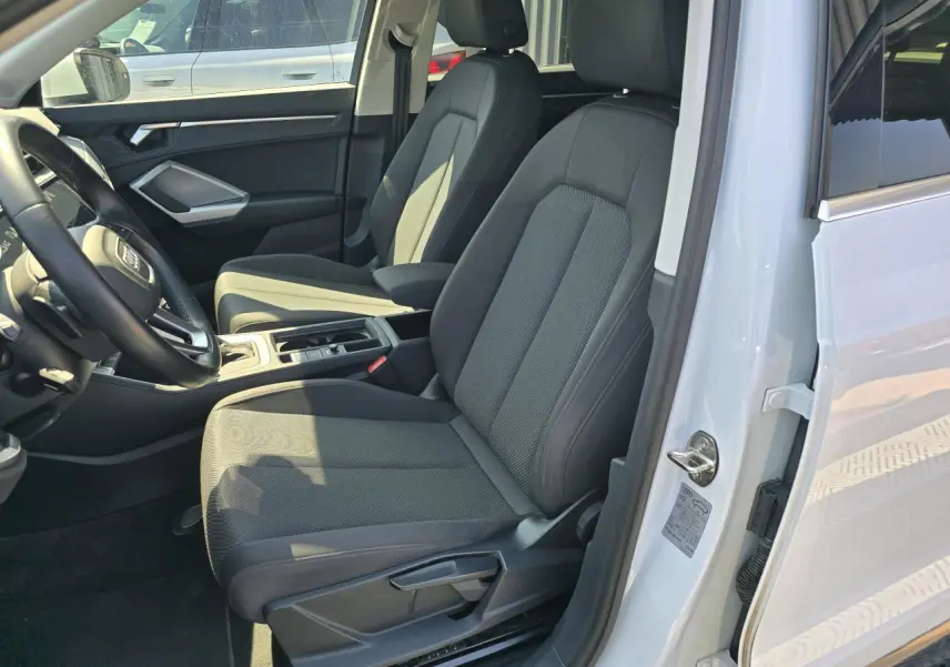 Vue intérieure côté conducteur de l'Audi Q3 blanc 2022, sièges tissu gris et volant multifonctions cuir.