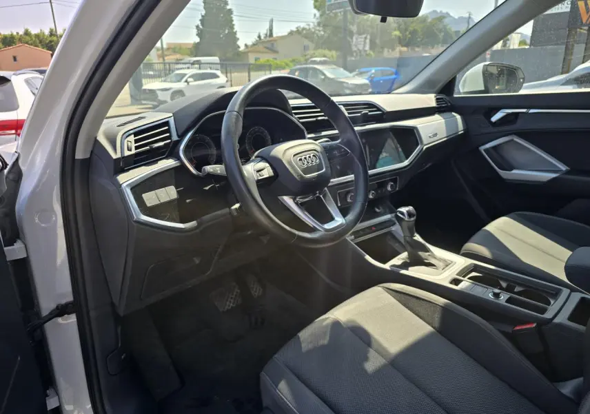 Vue intérieure côté conducteur de l'Audi Q3 blanc 2022, volant cuir multifonctions et tableau de bord moderne.