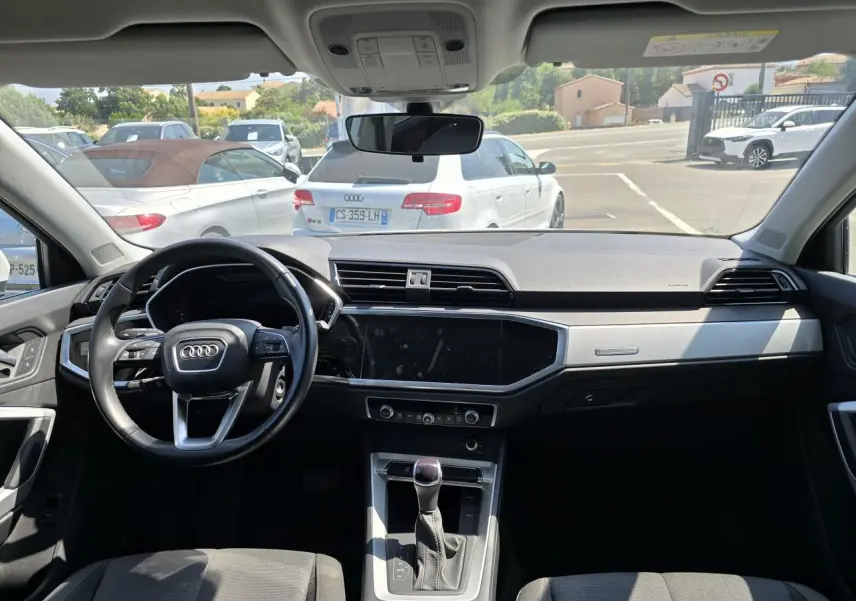 Vue intérieure avant de l'Audi Q3 2022, tableau de bord moderne avec volant cuir multifonctions et écran tactile central noir.