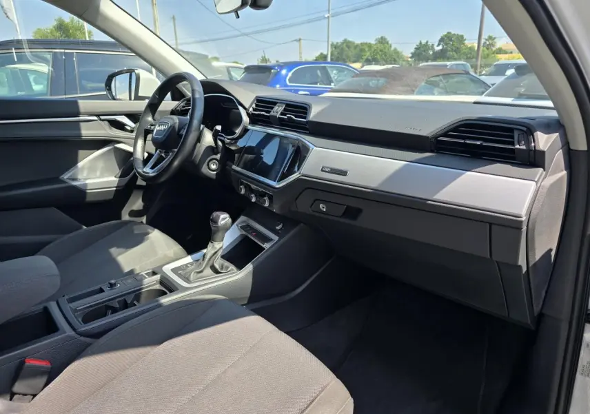 Vue intérieure côté passager de l'Audi Q3 blanc 2022, montrant tableau de bord moderne et volant multifonctions.