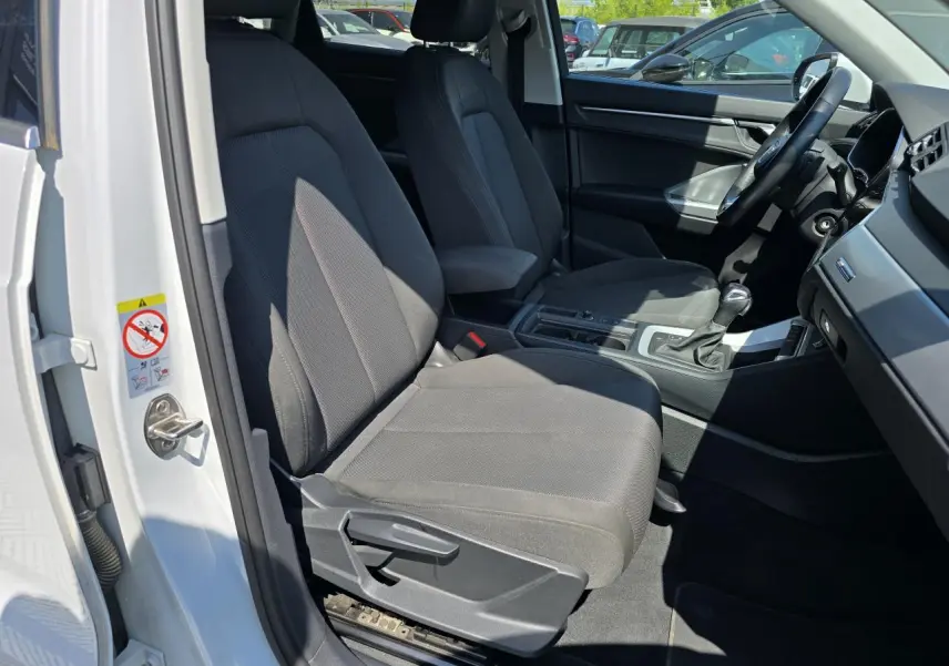 Vue intérieure côté conducteur de l'Audi Q3 blanc 2022, montrant les sièges avant et la console centrale.