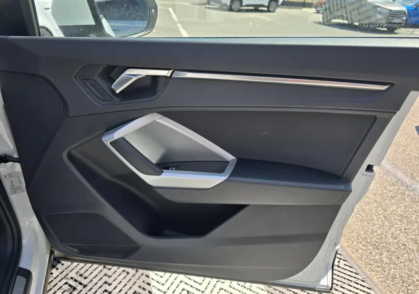 Vue intérieure de la porte avant gauche blanche d’un Audi Q3 2022 avec garniture noire et insert argenté.