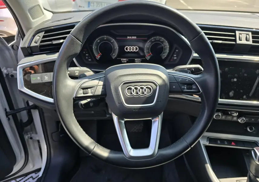 Vue intérieure centrée sur le volant cuir multifonctions de l'Audi Q3 blanc avec tableau de bord digital.