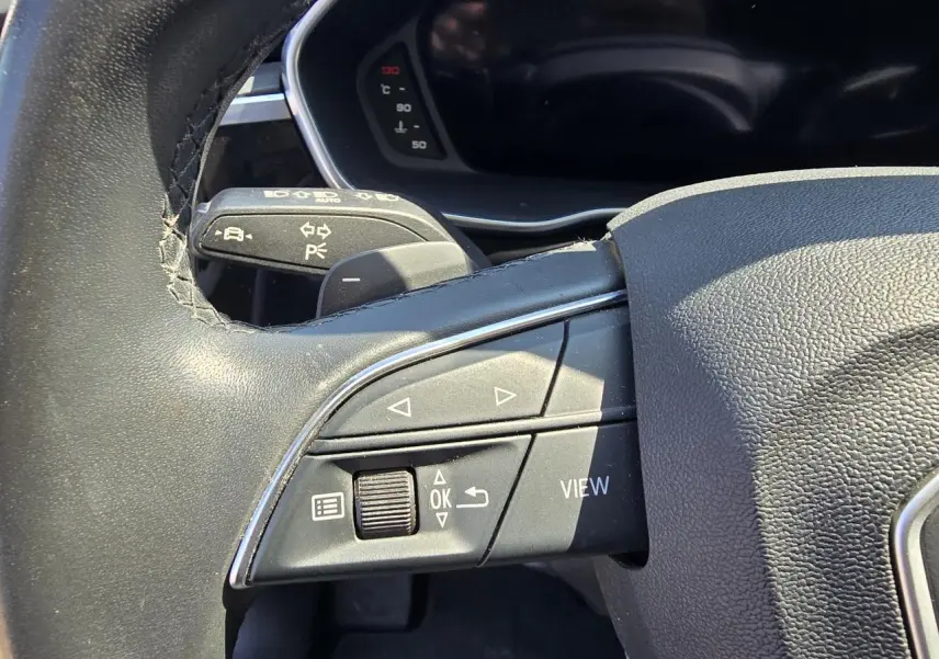 Gros plan sur les commandes gauche du volant cuir de l'Audi Q3 blanc, avec boutons multifonctions et palettes au volant.
