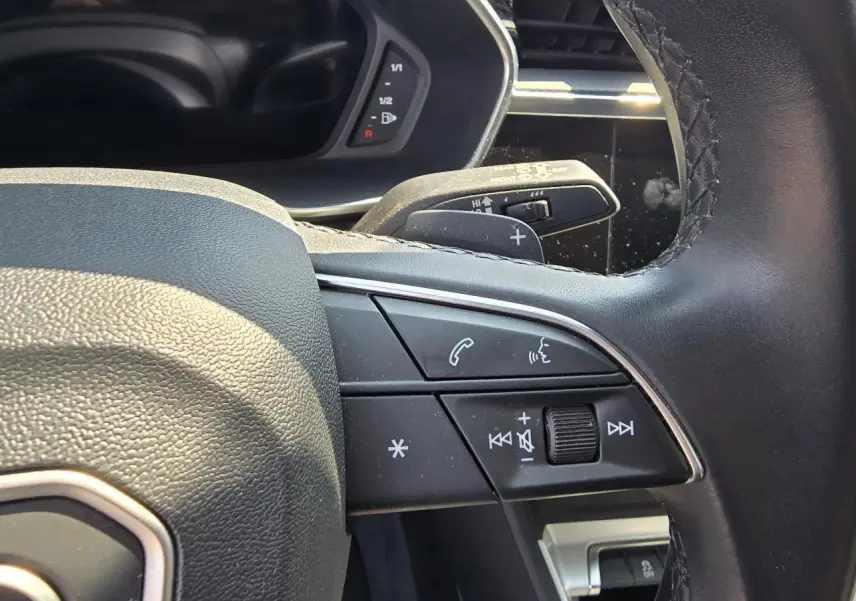 Gros plan sur le volant multifonctions en cuir de l'Audi Q3 2022, avec commandes audio et palettes au volant.