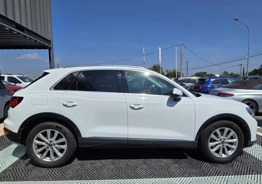 Audi Q3 blanc vue de profil côté gauche avec jantes aluminium 5 branches doubles et vitres arrière surteintées.