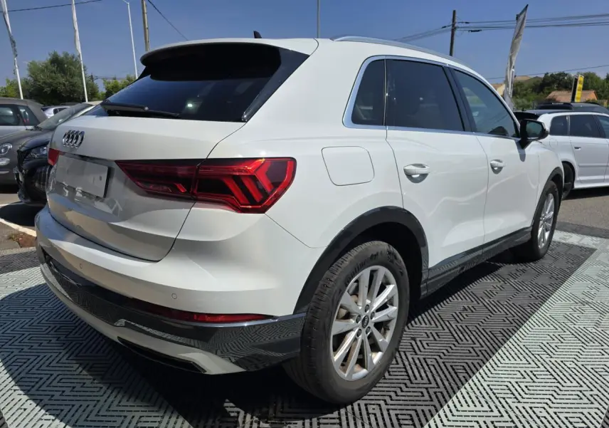 Audi Q3 blanc vue 3/4 arrière droit avec vitres surteintées et jantes aluminium 5 branches doubles.