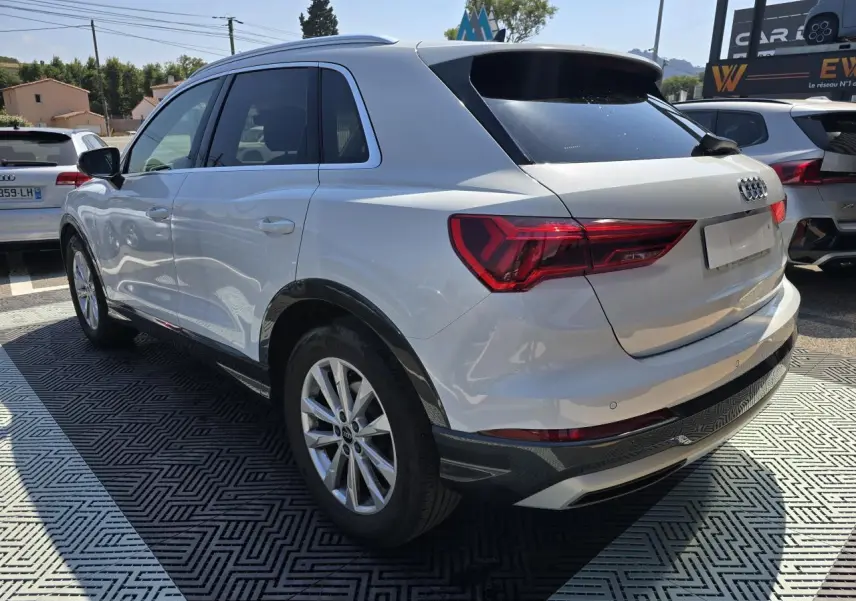 Audi Q3 blanc vue 3/4 arrière droit avec vitres surteintées et jantes aluminium 5 branches doubles.