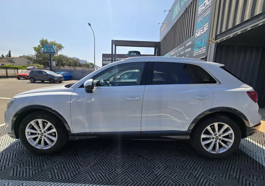 Vue de profil côté gauche d'un Audi Q3 blanc avec jantes aluminium 5 branches doubles et vitres arrière surteintées.