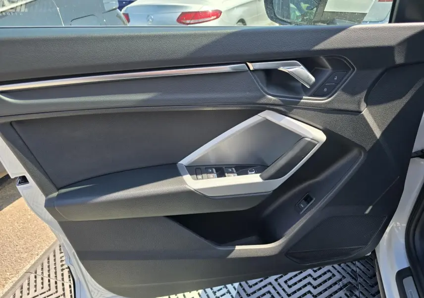Vue intérieure de la porte avant gauche blanche de l’Audi Q3 2022 avec commandes de vitres et poignée argentée.