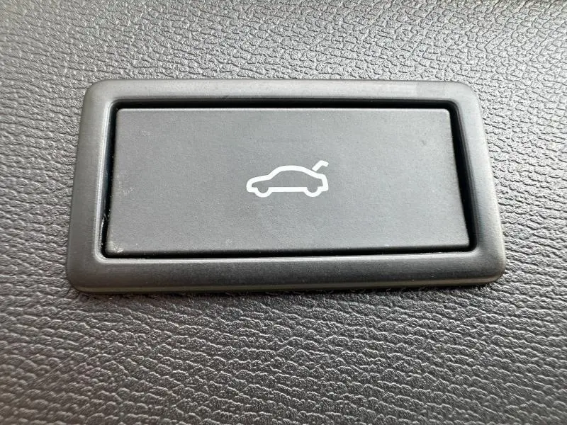 Bouton noir avec pictogramme blanc d'ouverture de coffre, sur tableau de bord texturé du CUPRA Formentor blanc Nevada.