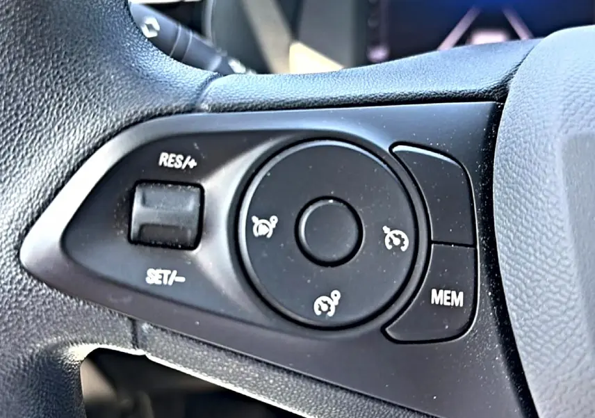 Gros plan sur les commandes de régulateur de vitesse au volant noir de l’Opel Corsa 1.2 turbo 100 edition.