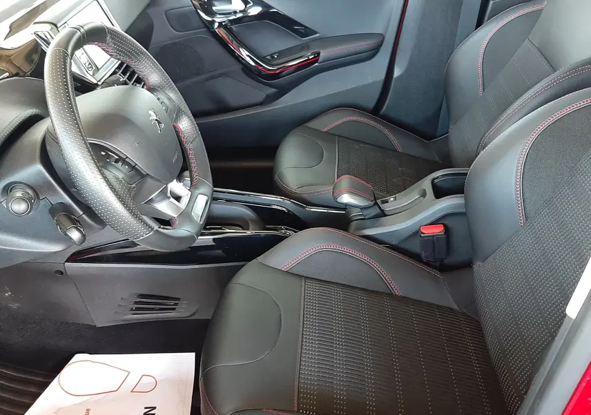 Vue intérieure côté conducteur du Peugeot 2008 rouge Ultimate Metal 2019, sièges noirs avec surpiqûres rouges et volant cuir perforé.