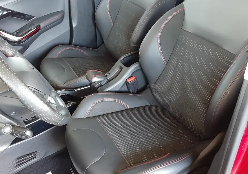 Intérieur avant du Peugeot 2008 rouge Ultimate Metal, sièges noirs avec surpiqûres rouges et volant perforé visible.