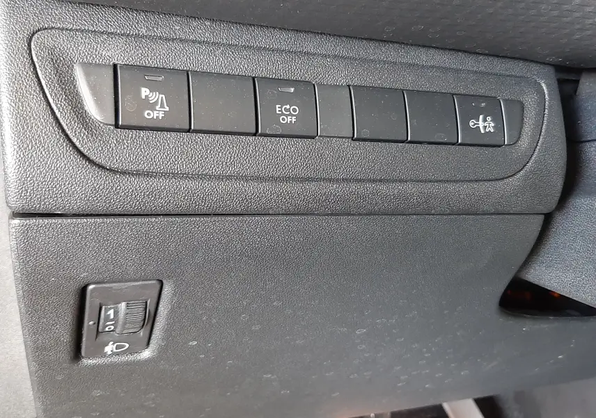 Gros plan sur les commandes de fonctions et réglage des phares sous le tableau de bord d'une Peugeot 2008 GT Line 2019.