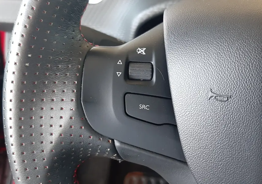 Gros plan sur la commande sonore du volant en cuir perforé avec surpiqûres rouges d'une Peugeot 2008 rouge Ultimate Metal 2019.