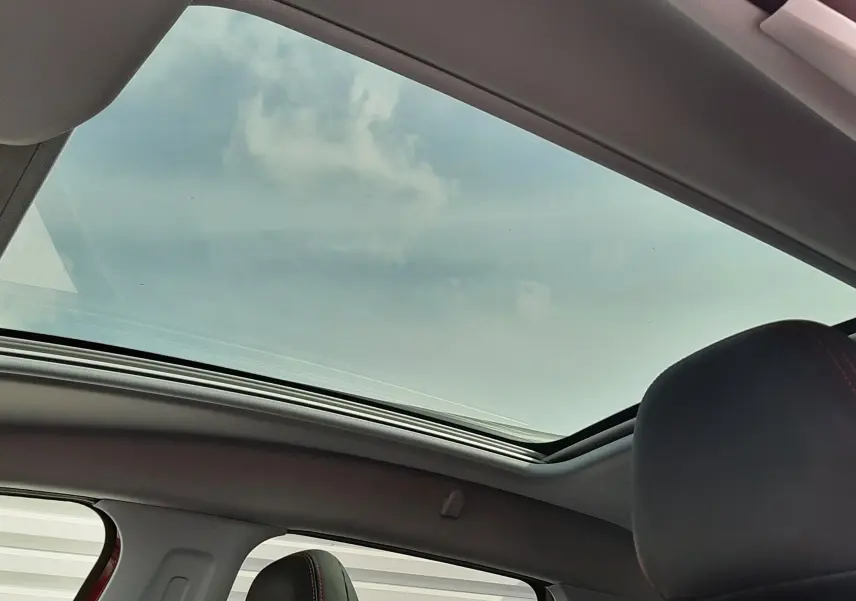 Toit panoramique ouvert sur l'intérieur noir d'un Peugeot 2008 rouge Ultimate Metal, vue depuis l'arrière côté droit.