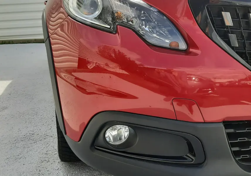 Gros plan sur l'avant droit rouge Ultimate Metal du Peugeot 2008 GT Line, mettant en valeur le phare et le antibrouillard.