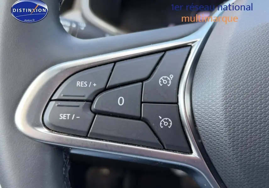 Gros plan sur les commandes de régulateur de vitesse au volant d'une Renault Clio V gris foncé.