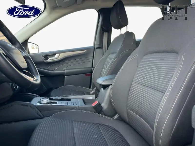 Vue intérieure côté conducteur du Ford Kuga 2023, sièges sport noirs avec accoudoir central et volant cuir multifonction.