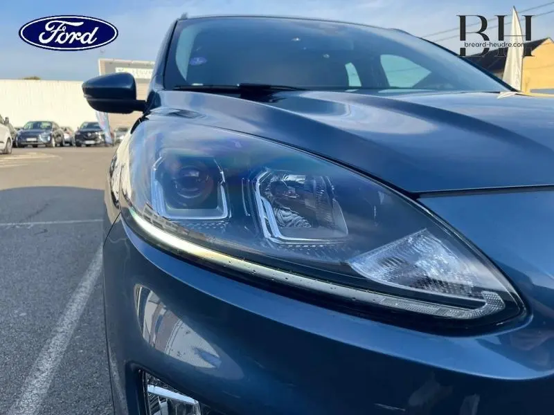 Gros plan sur le phare avant gauche du Ford Kuga 2023 bleu azur métallisé, mettant en valeur ses lignes modernes et LED.