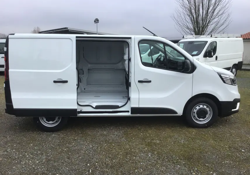 Vue de profil côté droit d’un Renault Trafic fourgon blanc avec porte latérale coulissante ouverte montrant l’espace de chargement vide.