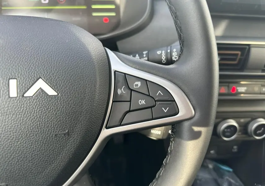 Gros plan sur les commandes au volant du DACIA Jogger 2025, avec tableau de bord et console en arrière-plan.